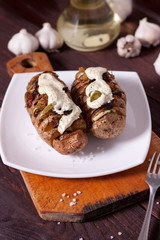 Baked potato with onions and spices on a white dish on the background of a wooden table