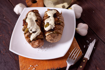 Baked potato with onions and spices on a white dish on the background of a wooden table
