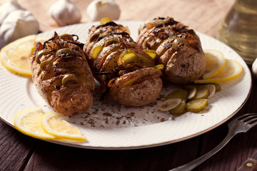 Baked potato with onions and spices on a white dish on the background of a wooden table