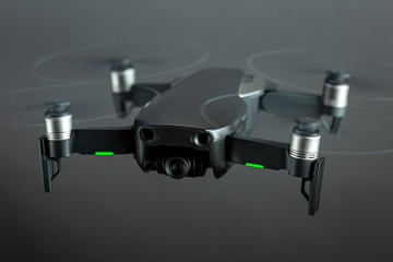 Drone in flight with spinning propellers and green positioning lights on seen from above against a grey even studio background
