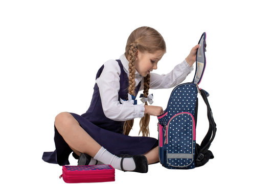seven-year-old girl schoolgirl in school uniform opens school backpack on white background