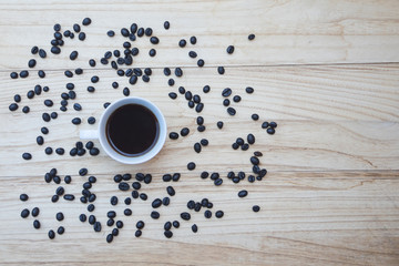 Top view of a white cup of fresh coffe on a wooden background with coffee beans