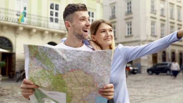 Couple With Map On Travel Vacations, Sightseeing. Happy Tourist Man And Woman In Stylish Clothes Traveling On Weekend, Walking With Map Around Streets. Tourism Concept. High Quality Image.