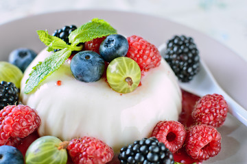 Delicious cream Panna Cotta dessert decorated with various berries mint leaves are at a plate on a table, macro