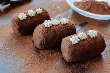 Delicious chocolate brownie as a potato form, Russian traditional dessert, on a dark desk and cacao powder on it, close up