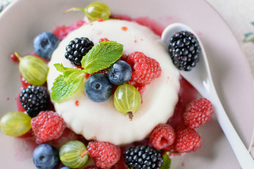 Delicious cream Panna Cotta dessert decorated with various berries mint leaves are at a plate on a table, closeup, top view