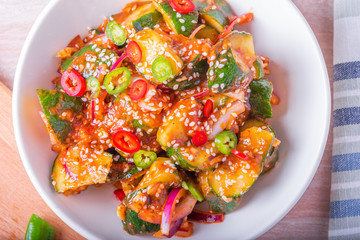 Oi Muchim Korean spicy cucumber salad with sesame seeds and chopped chili in a bowl on a wooden table close-up, top view.