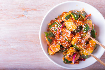 Oi Muchim Korean spicy cucumber salad with sesame seeds in a bowl on a wooden table, copy space, top view.