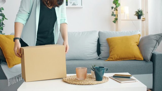 Girl comes home after work with a cardboard box and tiredly sits on the sofa. 4k slow motion footage.
