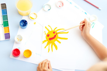 Child's hand draw  dips the brush into watercolor paint to draw a pattern with sun