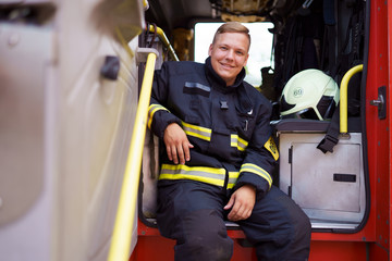 Image of smiling fireman sitting in fire truck at fire station