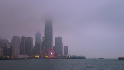 Time lapse day to night of Hong Kong cityscape with hard mist at the harbor in the raining day