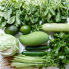 Fresh green vegetables variety on rustic white background from overhead, celery, avocado, cabbage, mango, cucumber, spinach, lime, squash. Healthy, vegetarian concept. Flat lay, top view