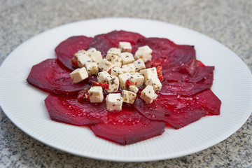 Baked and sliced beetroot served on simple white plate as light vegetarian salad or appetizer with soft cubes of marinated greek style feta cheese with herbs and sea salt.