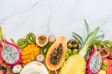 Fresh exotic fruits and tropical palm leaves on white marble background - papaya, mango, pineapple, passion fruit, dragon fruit, melon. Mockup, flat lay, overhead. Top view.