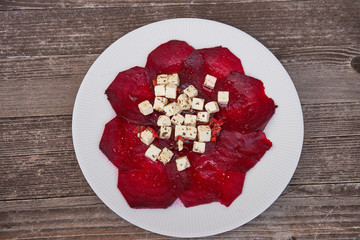 Top view on sliced baked beetroot appetizer salad with soft cubes of feta cheese with herbs, apple vinegar and sea salt on white plate and vintage wooden table. Light dish for weight reduction diet.