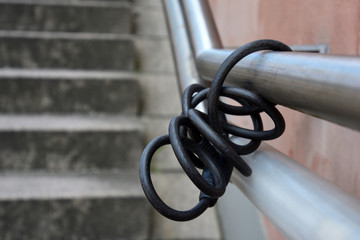 Black bike lock attached to metal railing at public stairs leading to train station with bicycle...