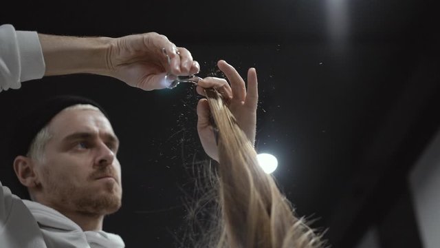 A middle plan of a male hairdresser cutting a lock of blonde hair