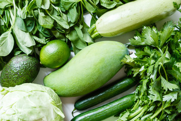 Fresh green vegetables variety on rustic white background from overhead, celery, avocado, cabbage, mango, cucumber, spinach, lime, squash. Healthy, vegetarian concept. Flat lay, top view