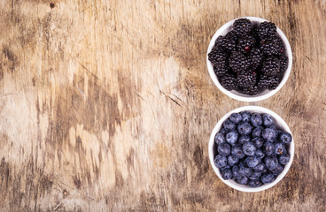 Blueberries and blackberries on wooden background. Wild berries in white bowls. Blueberries and blackberries copy space