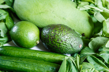 Fresh green vegetables variety on rustic white background from overhead, celery, avocado, cabbage, mango, cucumber, spinach, lime, squash. Healthy, vegetarian concept. Flat lay, top view