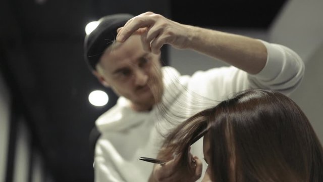 A male hairdresser divides, combs and cuts an overflowing brown forelock