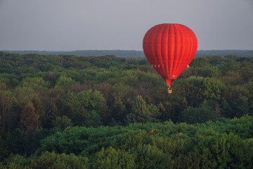 Red hot air balloon in the sky above the trees