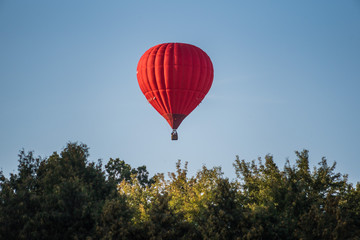 Red hot air balloon in the sky above the trees