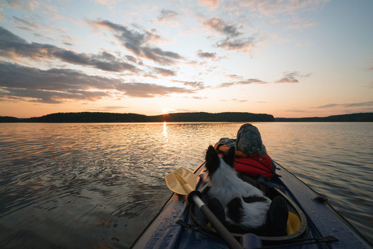 The hostess and the dog are sailing on the lake in a kayak boat at sunset .
