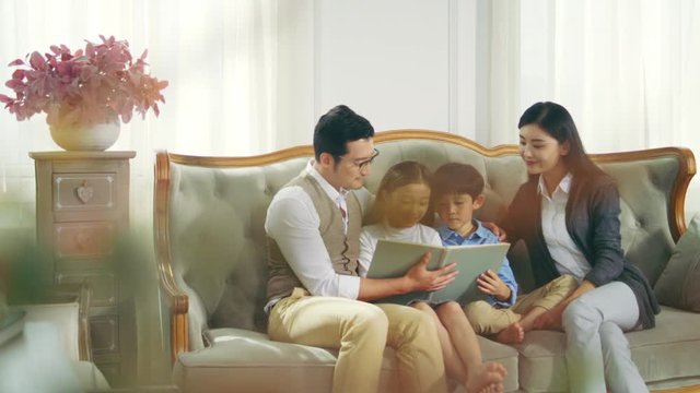 asian family with two children reading book together in living room at home