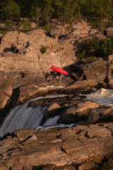 Red Kayak Being Carried on a Rocky River Bank with Whitewater and Waterfall on a Sunny Morning in the Summer at Great Falls Park