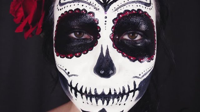 Halloween mask Catrina. Mexican day of the dead. Portrait of a young woman with scary makeup for Halloween on a dark background. 4K