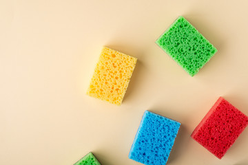 Yellow, green, red, blue sponges on cream colored paper background, copy space, top view, flat lay