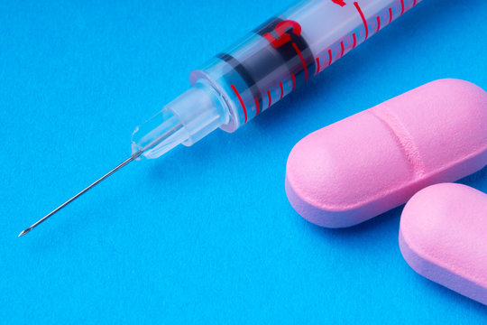 1ml insulin syringes and pink pills on a blue background. omega3.