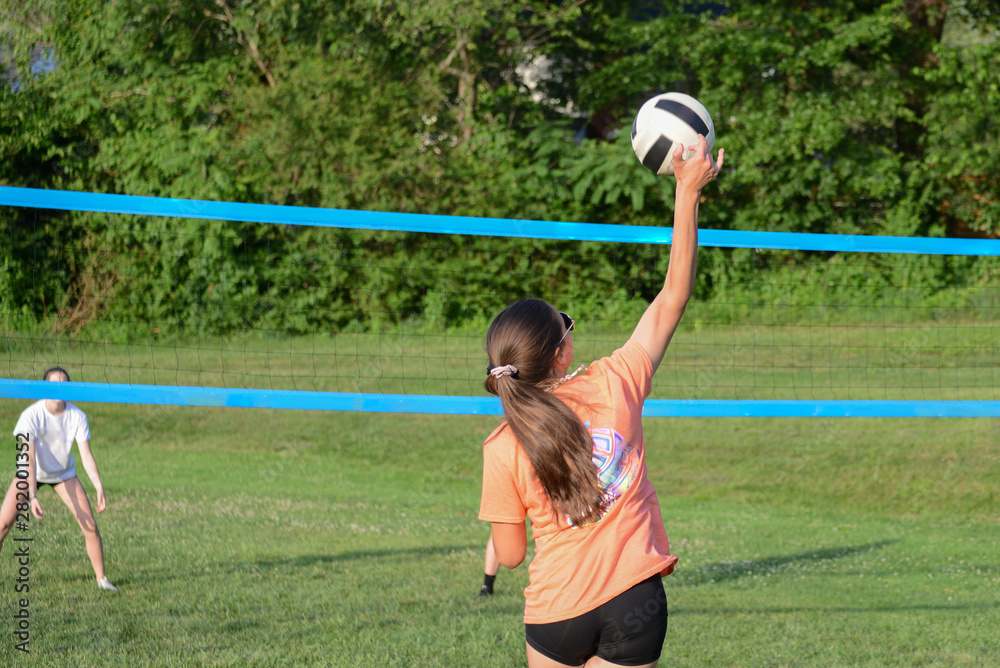 Poster girl serving volleyball on outdoor grass field