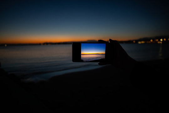 human hand holding a phone taking a picture of a sunset