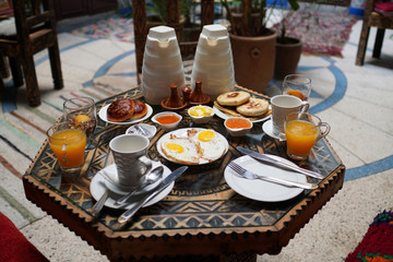 Moroccan breakfast on the table: eggs, fresh orange juice, green tea, pancakes, butter, honey and chocolate mousse.