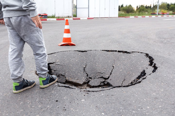 Little boy on the edge of a large pit in the road surface. A hole in the pavement. Need for highway...