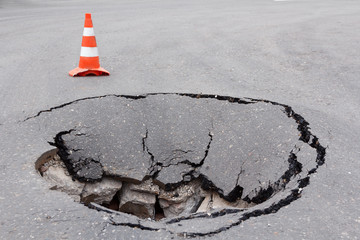 Deep sinkhole on a street city and orange traffic cone. Dangerous hole in the asphalt highway. Road...