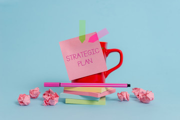 Writing note showing Strategic Plan. Business concept for A process of defining strategy and making decisions Coffee cup pen note banners stacked pads paper balls pastel background