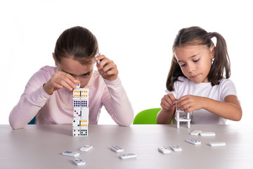 Two young girls of different ages playing with dominoes, concept of teamwork or unjust competition