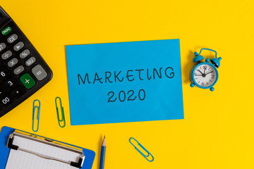 Handwriting text Marketing 2020. Conceptual photo Commercial trends for 2020 New Year promotional event Clipboard sheet clips note calculator pencil alarm clock colored background
