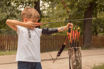 Boy with bow and arrow concentrated on target. Kid stared at target. Child directed arrow at a...