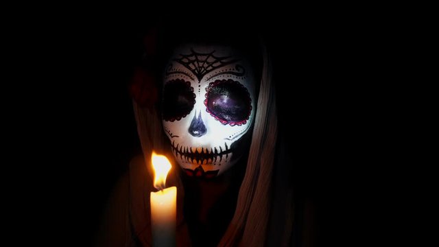 Halloween mask. Girl with candles in the flame of light. Mexican day of the dead. Portrait of a young woman with scary makeup for Halloween on a dark background. 4K