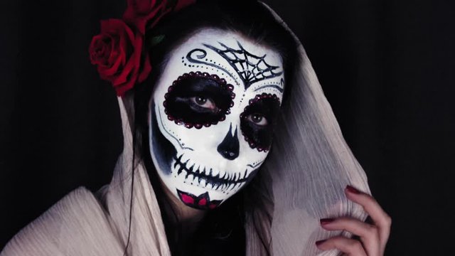 Halloween mask Catrina. Mexican day of the dead. Portrait of a young woman with scary makeup for Halloween on a dark background. 4K