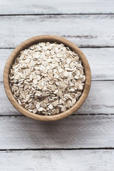 Uncooked oatmeal or oat flakes in a wooden bowl on a white wooden background