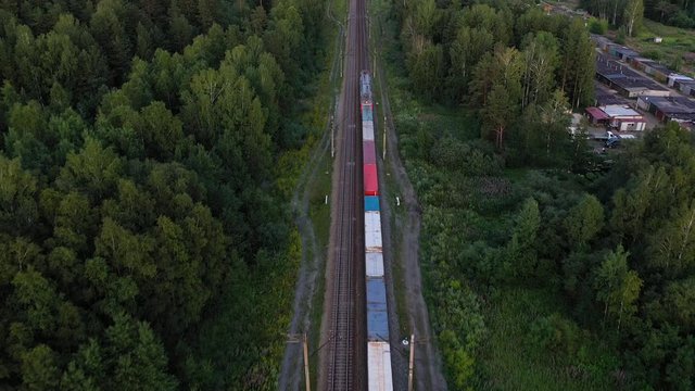 Aerial view of the freight train, carrying rubble and cement, moving through the forest at sunset. 4K footage from drone