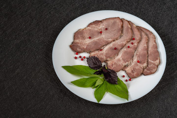 Baked meat cut into pieces on a white plate with basil and red pepper grains close-up top view on a black background