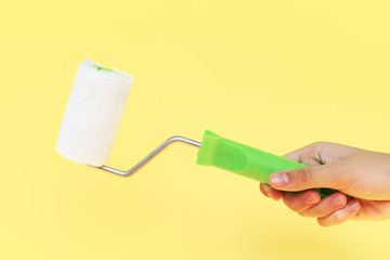 Female hand holding paint roller isolated over yellow background