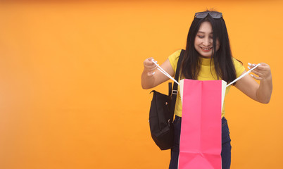 Isolated shot of pretty adult woman with shopping bag, wears casual outfit, dressed casually, Beautiful Asian models over yellow background for advertising concept